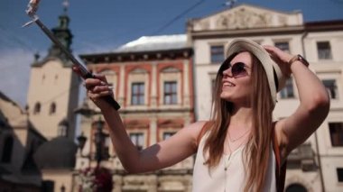 Güzel, genç bir bayan gülümsemesi şehirde neşeli bir selfie çekerken eğleniyor.