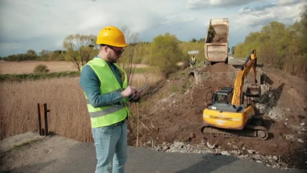 Construcción del puente. Ingeniero de carretera en uniforme de seguridad, un joven ingeniero barbudo — Vídeo de stock