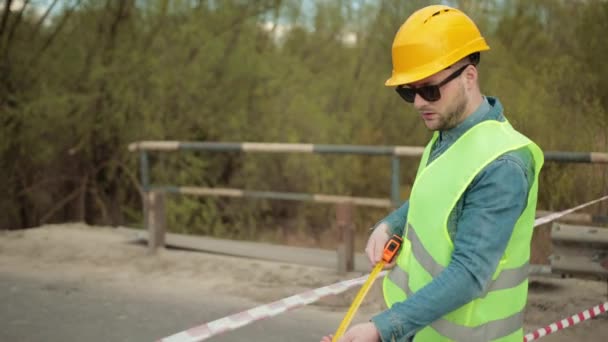 Vousatý inženýr v ochranné přilbě páska opatření v ruce měří vzdálenost — Stock video