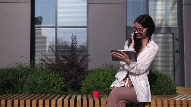 Młoda kobieta korzystająca z tabletu cyfrowego na zewnątrz, przy użyciu tabletu cyfrowego, pijąca kawę — Wideo stockowe