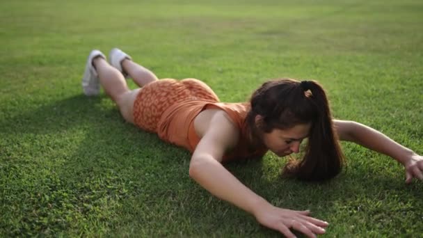 フィットネス初心者のための運動。公園で膝の腕立て伏せをしている若い女性. — ストック動画