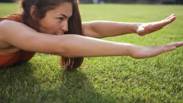 Mujer sexy acostada en la hierba verde. Fitness mujer piso ejercicio mueve las manos. — Vídeos de Stock