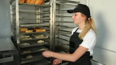 Baker hamur tepsisini raftan, çöreklerden ve krakerlerden bir fırından alır.