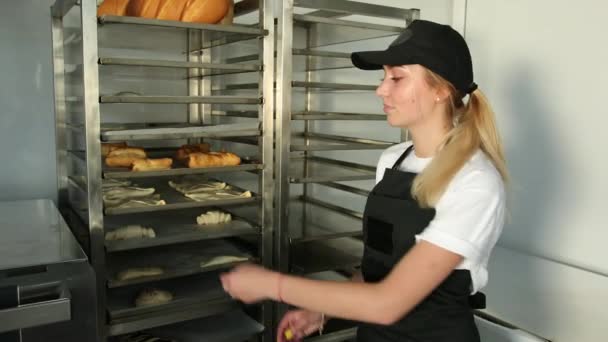 Пекарь берет поднос для теста из стойки, булочек и кренделей в духовку в пекарне — стоковое видео