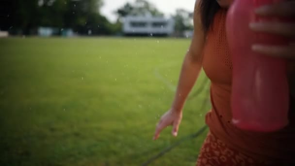 Acercamiento mujer beber agua en la puesta del sol, joven atleta en naranja camiseta — Vídeo de stock