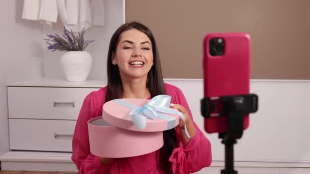 Jonge vrouwelijke influencer uitpakken van grote kartonnen doos, zitten mobiele telefoon — Stockvideo