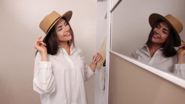 Una joven sonriente probándose el sombrero en la tienda. Feliz hermosa chica eligiendo sombrero — Vídeos de Stock