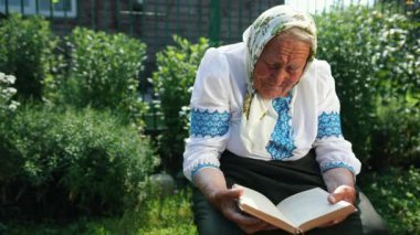 Yaşlı bir büyükanne sokakta oturuyor ve bir kitap okuyor. Vyshyvanka