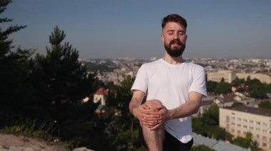 Yoga pozu, yoga dengesi, şehir arkaplanı. Panoramik şehir manzaralı tepede, genç adam mor minder üzerinde yoga yapıyor, konsantrasyonu ve doğal çevrede sağlıklı yaşamı vurguluyor..