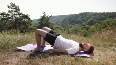 Yoga enerjisi, yoga, kişisel bakım, genç adam. Doğayla iç içe olan genç adam yoga dengesi kuruyor çimen tarlasında mor bir poz veriyor, beyaz tişört ve siyah şort giyiyor..