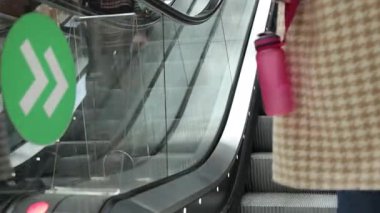 Yürüyen merdivenler, alışveriş merkezleri, yürüyen merdivenler. Modern alışveriş merkezlerinde yürüyen merdivenlere yakın çekim yapan insanların yeşil yönlü tabela ve giysi detaylarına odaklanması.