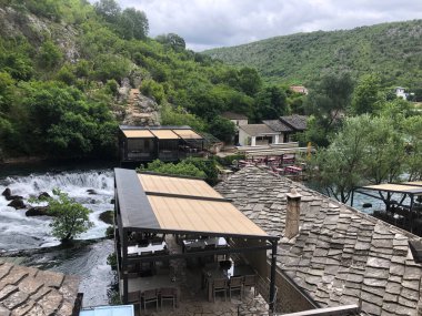 Blagaj 'daki Buna nehri şelalesinin yanında taş çatıları olan geleneksel nehir kenarı restoranı..