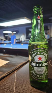 Bilardo salonundaki bilardo salonundaki bir bar masasında bira şişesi. Arka planda hafifçe bulanık masalar, gece keyfi, kapalı mekan eğlencesi ve markalı içecek tüketimini gösteriyor. 28 Ekim 2024