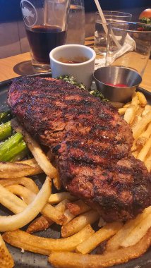 Kızarmış biftek, patates kızartması, sebze ve sosla servis edilir. İçten bir akşam yemeği ve klasik konforlu yemek sunumu vurgulanır..