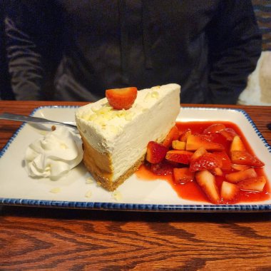 Lokanta tabağında taze çilek, çilek sosu ve krem şanti ile servis edilen kremalı pasta klasik bir tatlı sunumu ve tatlı yemek deneyimi sunar..