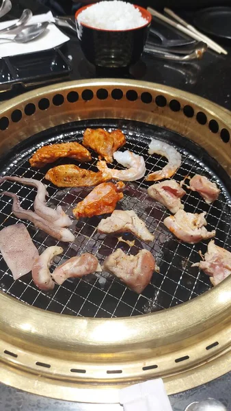 Masa başı ızgarasında karides, kalamar ve tavuk parçalarıyla birlikte çeşitli deniz ürünleri ve et ızgarası bir restoranın yemek düzeninde açık ateşte pişiyor..