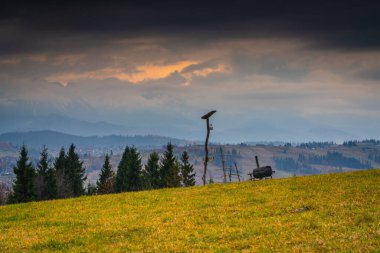 Ahşap yapısı ve tarım ekipmanlarıyla kırsal yamaçlar, sonbahar otlakları ve dramatik bulutların altında katmanlı dağlar, atmosferik hava ile geleneksel kır manzarası