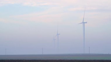 Günümüz rüzgâr türbinleri açık tarım arazilerinde yavaş yavaş yoğun sise dönüşerek sürdürülebilir enerji üretimini ve kırsal alanların minimalist bileşimini resmediyor.