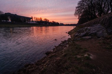 Uzh Nehri Ukrayna 'nın Uzhorod kentinden akar, şehrin ufuk çizgisi ve ağaçlarının üzerinde gün doğumunun canlı renklerini yansıtır.