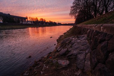 Uzh Nehri Ukrayna 'nın Uzhhorod kentinden akar ve şehrin ufuk çizgisi üzerinde çarpıcı bir günbatımı gökyüzünün canlı renklerini yansıtır.