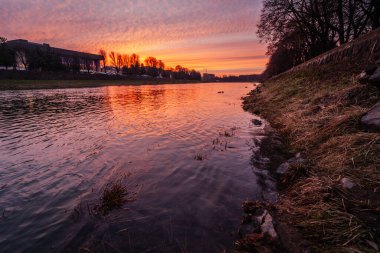 Ukrayna 'nın Uzhhorod kentindeki Uzh Nehri' nin üzerinde, sakin sulara ve çevresini çevreleyen manzaraya sıcak bir parıltı saçan çarpıcı bir günbatımı gökyüzünü alevli renklerle boyar.