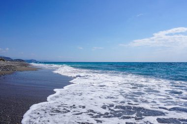Ege Denizi 'nin berrak mavi gökyüzünün altında karanlık bir çakıl taşıyla buluşması, Türkiye kıyılarının doğal güzelliğini gözler önüne seriyor.