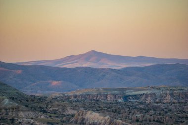 Kapadokya, Türkiye 'nin eşsiz jeolojik oluşumlarının ve yuvarlanan tepelerinin geniş manzarası gün batımının yumuşak ışığında yıkandı.