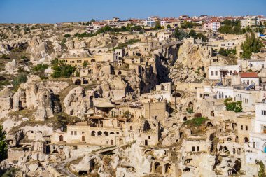 Panoramik bir bakış açısında, Türkiye 'nin Kapadokya kentinin kendine özgü jeolojik oluşumları ve tarihi mimarisi, antik mağara evleri ve çağdaş binaların karışımı yer alıyor.