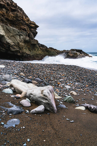 Dramatic volcanic rock formations meet the Atlantic Ocean on a secluded beach covered in dark pebbles and smooth stones