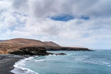 Fuerteventura 'daki engebeli Ajuy kıyı şeridi, turkuaz Atlantik Okyanusu dalgalarıyla karşılaşan karanlık volkanik kaya oluşumlarına sahiptir.