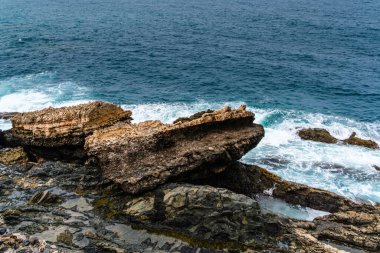 Karanlık volkanik kayaların dramatik jeolojik oluşumları, köpüklü beyaz dalgaların kıyıya vurduğu, turkuaz Atlantik Okyanusu ile buluşur.