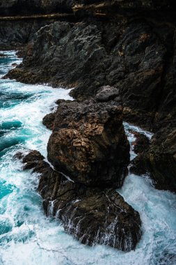 Fuerteventura 'daki Ajuy' un engebeli, karanlık volkanik kayalıkları güçlü, parlak turkuaz Atlantik Okyanusu dalgaları tarafından hırpalanır.