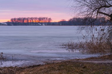 Polonya 'daki donmuş Dzierzgon Gölü' nün üzerinde nefes kesici bir günbatımı sırasında gökyüzü pembe ve turuncu renklerle patlar.