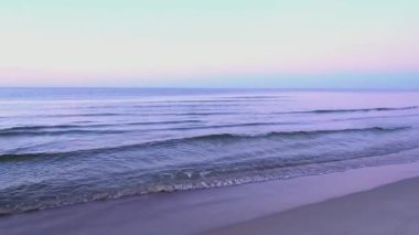 Sakin okyanus dalgaları yumuşak pastel bir gökyüzünün altında sakin kumlu bir sahile yuvarlanarak Baltık kıyılarının barışçıl atmosferini yakalıyor.