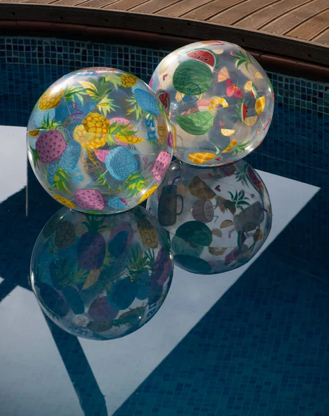 Havuzda yüzen iki yuvarlak renkli oyuncak top su yüzeyinde yüzüyor. Dikey eğlenceli su yansıması ile birlikte yaz gezisi hedefi görüntüsü. Geometrik şekiller, daireler ve havuz suyuna yansıyan dik açılar bayramı ya da yazı simgeliyor.