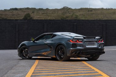 Gri Chevrolet Corvette C8 sarı işaretli asfalta park edilmiş, lüks spor araba tüm gövdesi bulutlu arka planda.