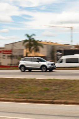 Gümüş Volkswagen T-Cross yan görüntüsü, şehrin bulanık arka planına sahip modern SUV sürüşü.