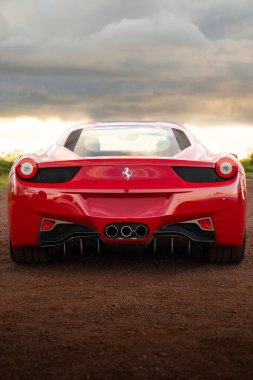 Kırmızı Ferrari 458 Italia arka görüş, lüks süper araba kirli tepenin üstünde üçlü egzoz boruları bulutlu günbatımının altında