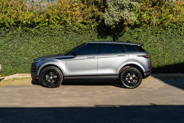 Gri Range Rover Evoque yan görüş profili, lüks SUV yeşil doğa arka planına sahip garaj yoluna park edilmiş.