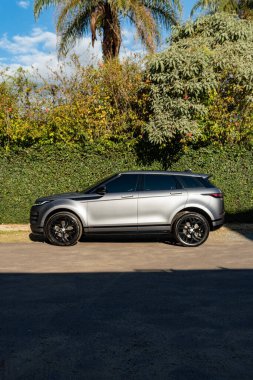 Gri Range Rover Evoque yan görüş profili, lüks SUV yeşil doğa arka planına sahip garaj yoluna park edilmiş.