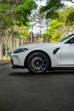 Beyaz BMW M3 müsabakası ön taraf görünümü, spor sedan tekerleği ağaç sıralı yola yakın