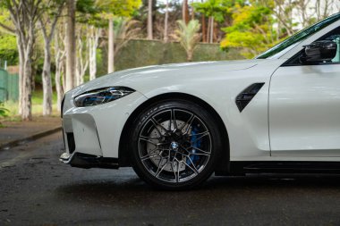 Beyaz BMW M3 müsabakası ön taraf görünümü, spor sedan tekerleği ağaç sıralı yola yakın