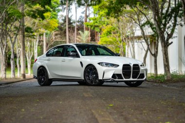 Beyaz BMW M3 müsabakası ön manzara üç çeyrek, uzun ağaçlı boş yolda lüks sedan.