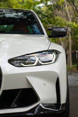 Beyaz BMW M3 müsabakası ön manzara yakın çekim, lüks spor araba farları ağaçlık yola yakın.