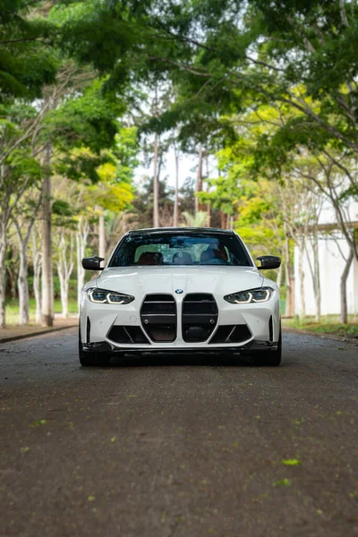 Beyaz BMW M3 Yarışma öngörüsü boş yol, spor sedan agresif tasarım, yeşil ağaçlar arka plan