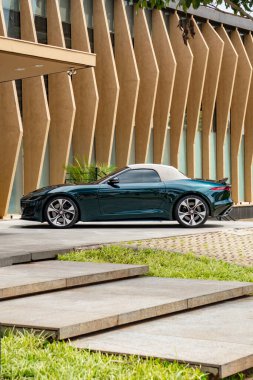 Yeşil Jaguar F tipi beyaz kapaklı, üstü açık spor arabası dışarıda park edilmiş.