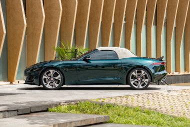 Yeşil Jaguar F tipi beyaz kapaklı, üstü açık spor arabası dışarıda park edilmiş.