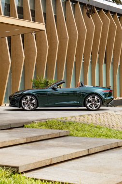 Koyu yeşil Jaguar F Tipi yan görünüm üstten aşağı, lüks lüks yol gösterici şehir yolunda park halinde.