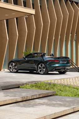 Yeşil Jaguar F tipi arka üç çeyrek manzara modern binanın yanına park edilmiş lüks bir spor araba.