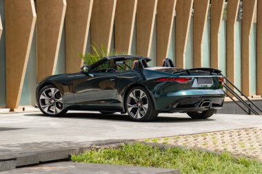 Yeşil Jaguar F tipi arka üç çeyrek manzara modern binanın yanına park edilmiş lüks bir spor araba.